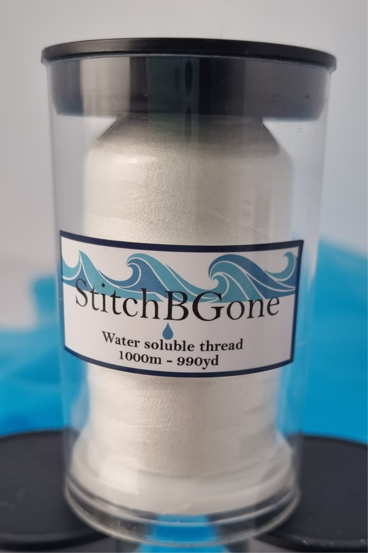 Spool of white thread with 'Stitch B Gone' label on a clear container against a blue and gray background