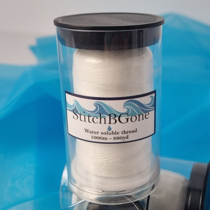 Spool of white thread in a clear container with 'Stitch B Gone' label on a blue background